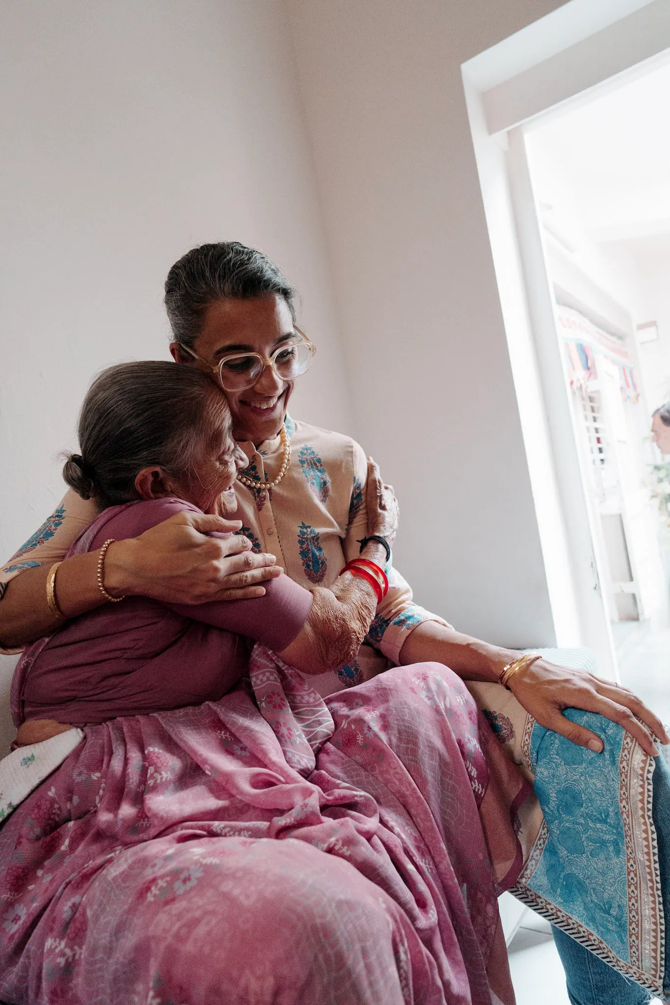 A woman embracing an elder family member near a bright window.