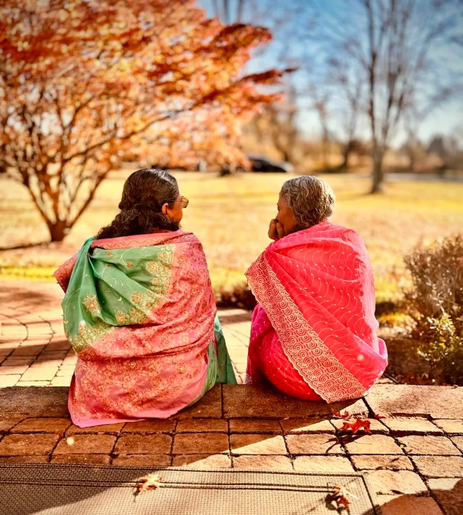 Two women in saris sitting together outside.