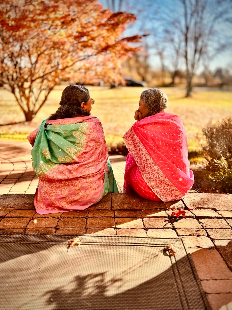 Two women in saris sitting together outside.